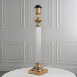 Endon Aldmont table lamp base with clear glass column and antique brass detailing on a square base, set on a marble table against a panelled wall.