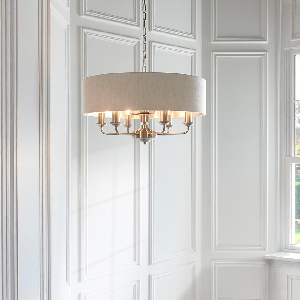Brenley 6 Light Pendant in white and chrome, a drum-shaped fabric shade over six candle-style arms, hanging from a chain in a panelled white room.