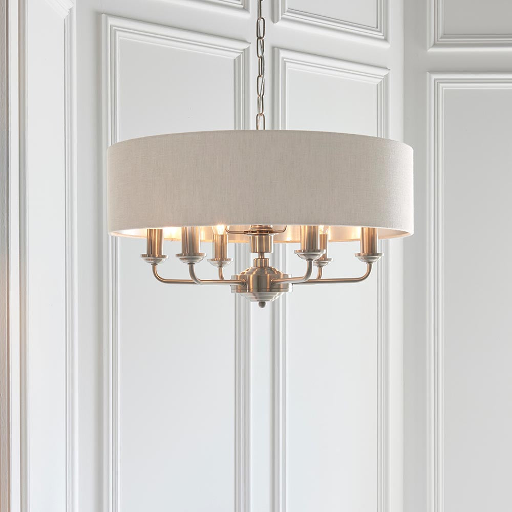 Brenley 6 light pendant with linen drum shade and nickel candle arms, hung on a chain in a panelled white hallway.