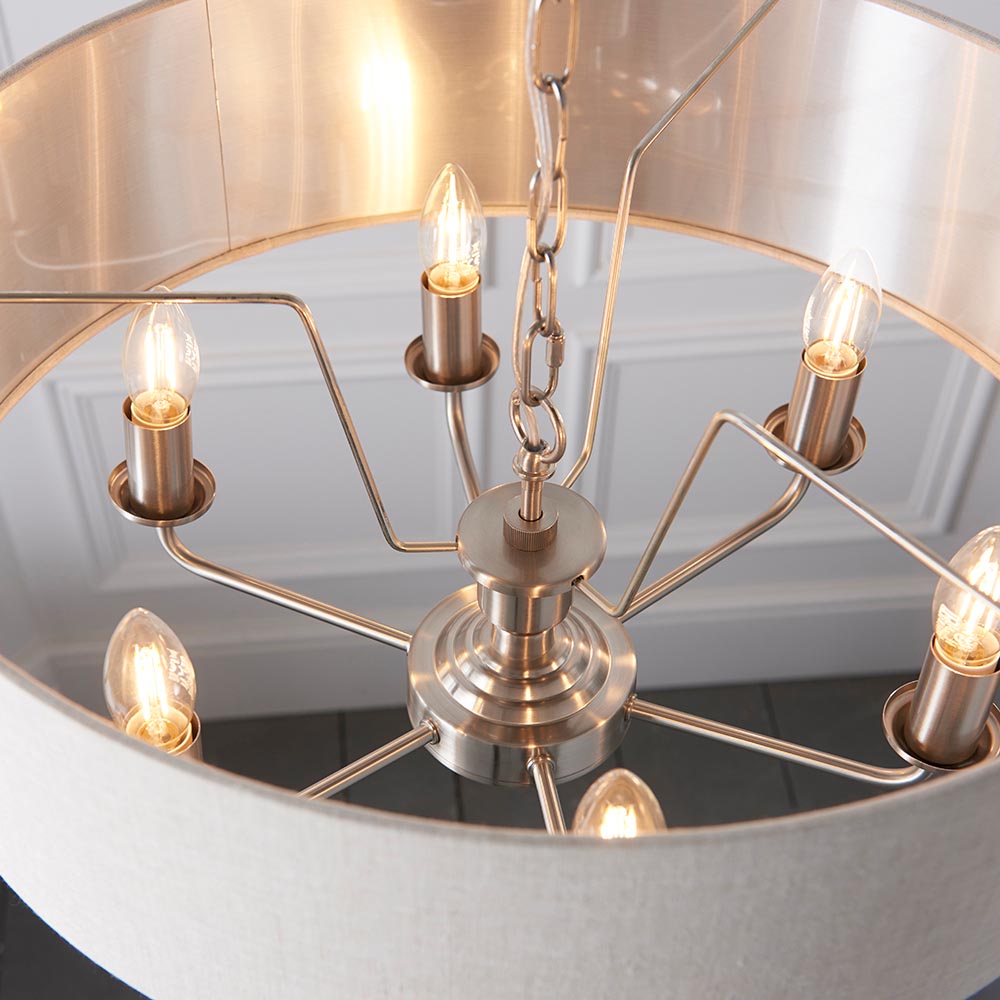 Brenley 6 Light Pendant in chrome, close-up of E14 candle bulbs on splayed arms beneath a linen shade with mirrored inner lining.