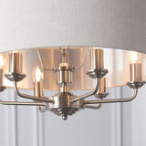 Close-up of the Brenley 6 light pendant showing brushed nickel arms, exposed E14 bulbs, and a linen shade with reflective metallic lining.