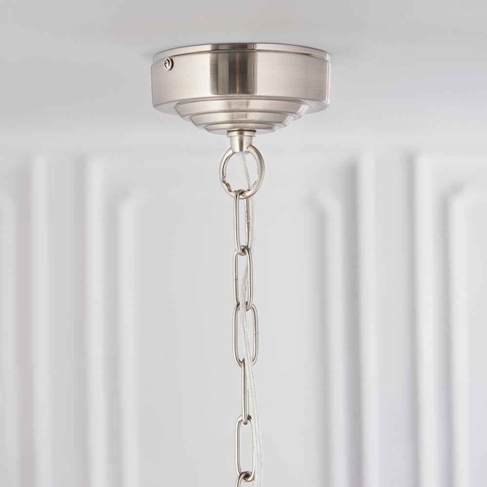 Close-up of the Brenley 6 Light Pendant's brushed nickel ceiling mount with adjustable chain and clear flex, set against a white panelled wall.