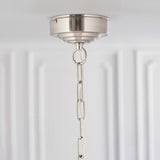 Close-up of the Brenley 6 Light Pendant's brushed nickel ceiling mount with adjustable chain and clear flex, set against a white panelled wall.