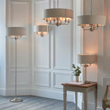 Brenley 3 Light Floor Lamp in brushed chrome with a wide linen drum shade, shown in a panelled living room alongside matching pendant and table lamps.