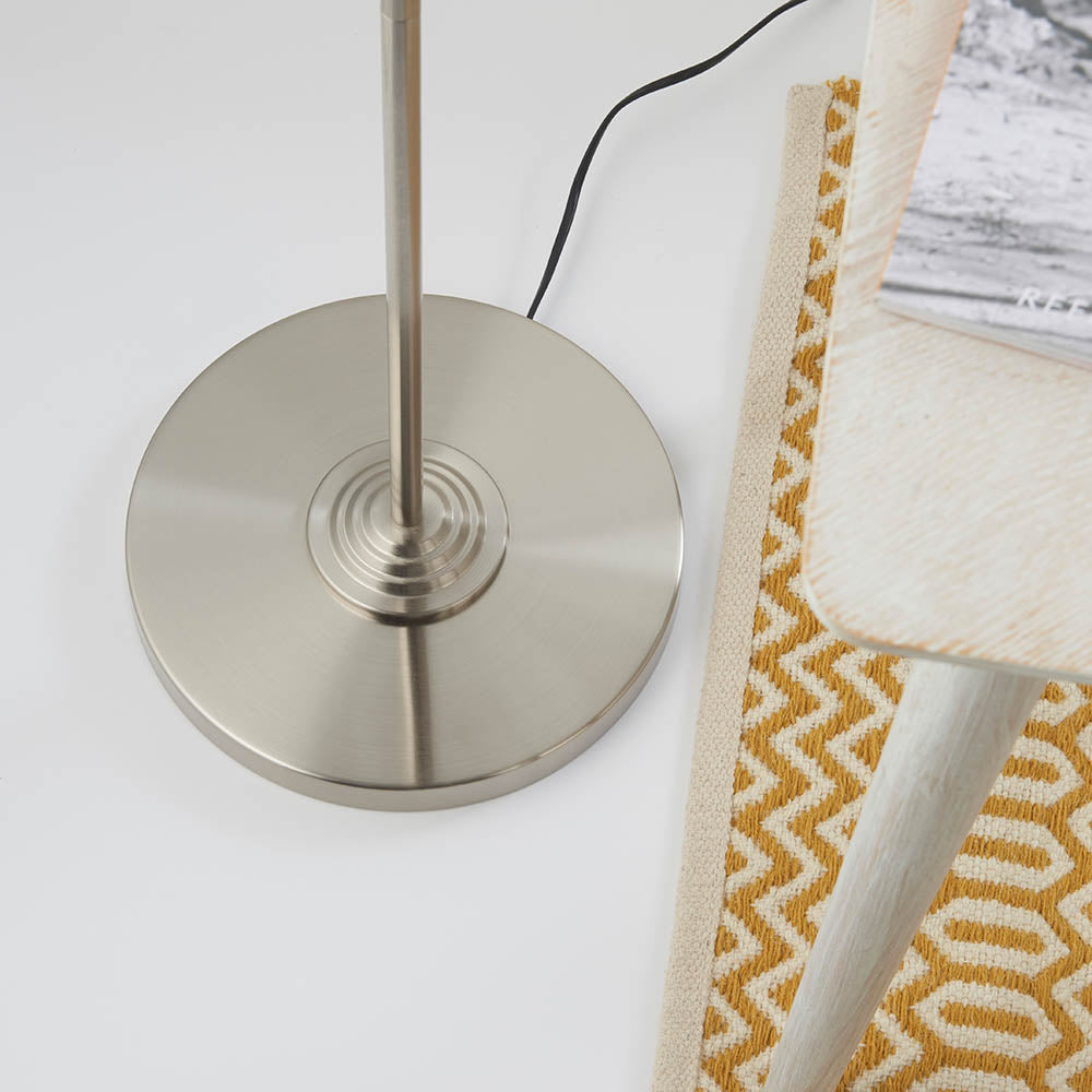 Brenley 3 Light Floor Lamp in brushed chrome, close-up of ridged circular base and stem beside a patterned rug and stool.