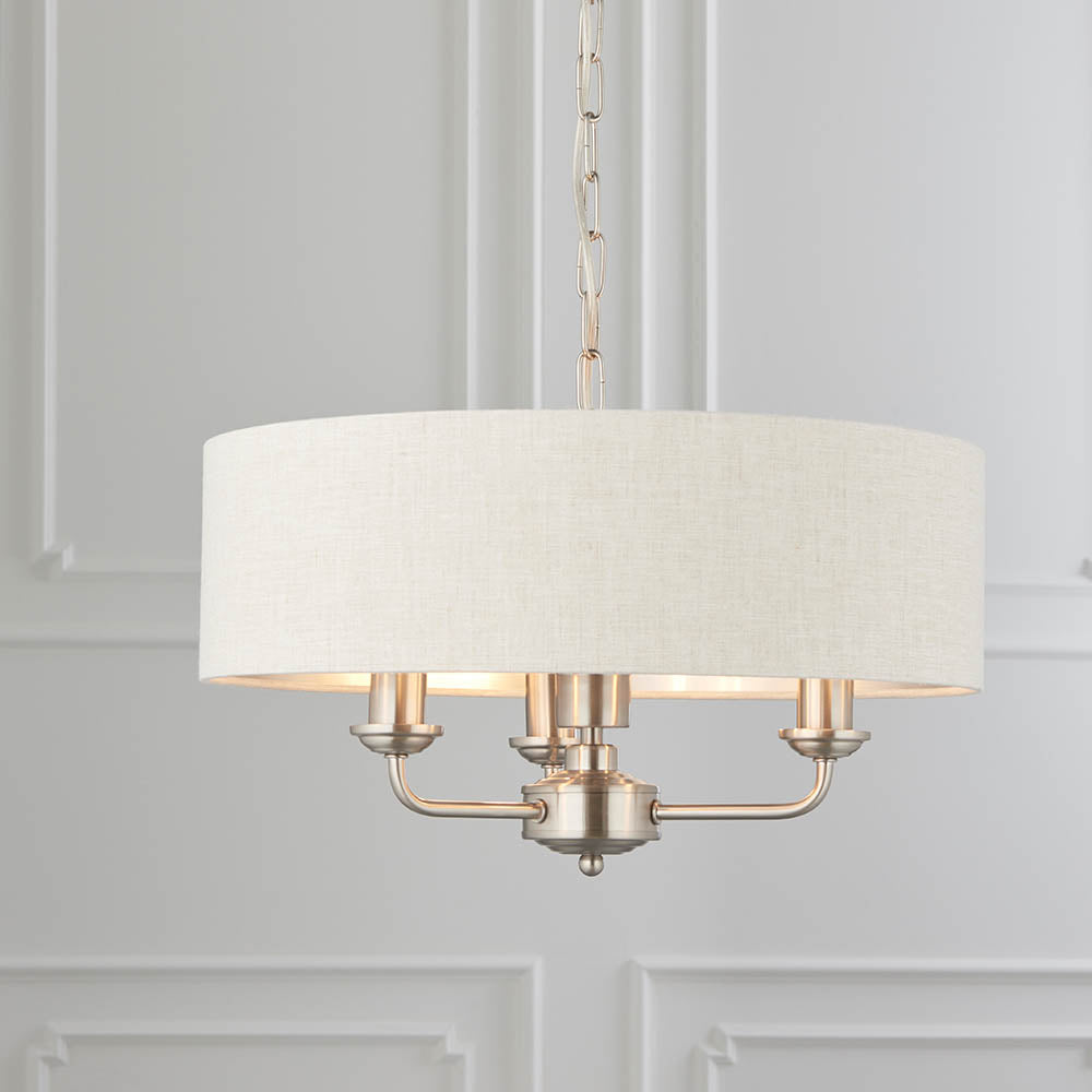Brenley 3-Light Pendant with white linen drum shade, brushed metallic lining, chrome fittings, and three exposed candle-style arms on a chain.