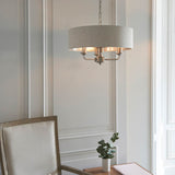 Brenley 3 Light Pendant with round linen fabric shade, brushed metallic lining, and chrome fittings, hung above a dining table in a light-toned room.