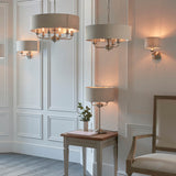 Brenley 3-light pendant with round taupe linen drum shades, chrome fittings and chain suspension, lit alongside matching wall lights and a table lamp.