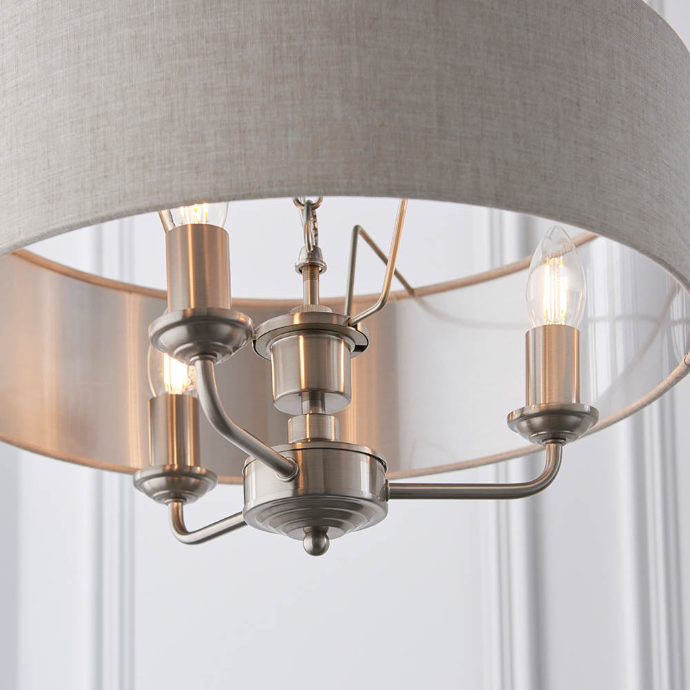 Brenley 3 Light Pendant close-up showing chrome candle-style arms with E14 bulbs beneath a grey linen drum shade with reflective inner lining.