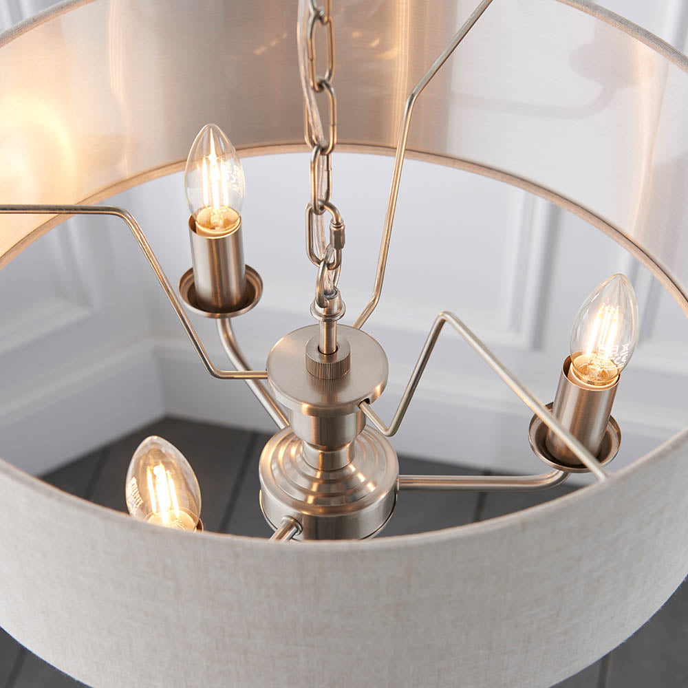 Close-up of the Brenley 3-Light Pendant with chrome candle-style fittings, lit bulbs, and chain suspension inside a white linen shade with mirrored lining.