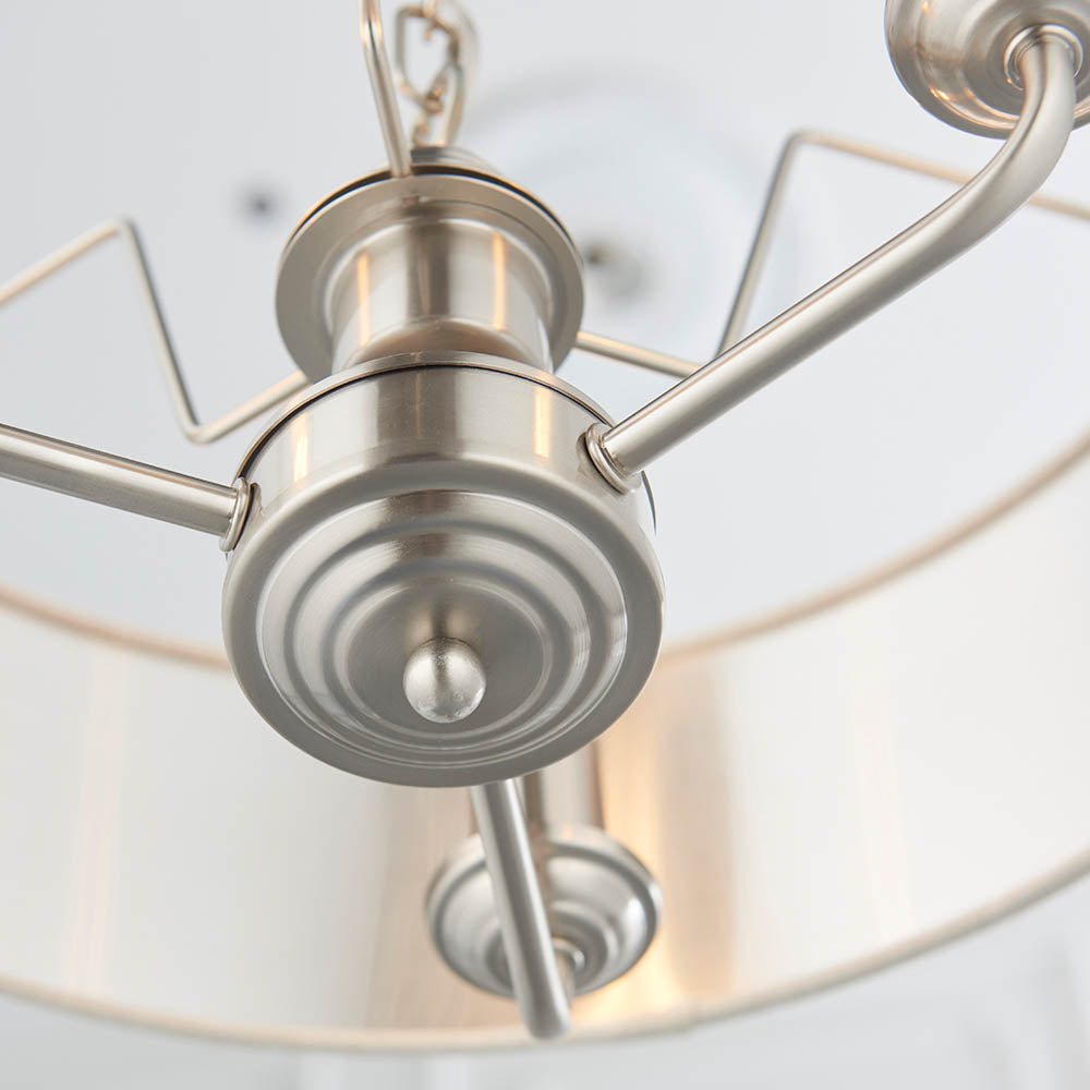 Close-up of the Brenley 3 Light Pendant's brushed nickel centre hub with three curved arms and adjustable chain, set against a white fabric shade.