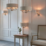 Endon Brenley 3 light table lamp with natural linen drum shade and brushed chrome stand, displayed with matching pendants and wall light in a panelled room.
