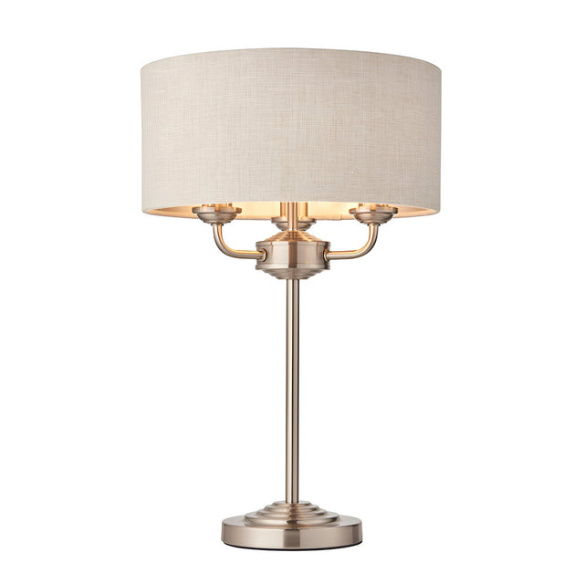 Endon Brenley 3 light table lamp with brushed chrome metalwork and natural linen drum shade on a plain white background.
