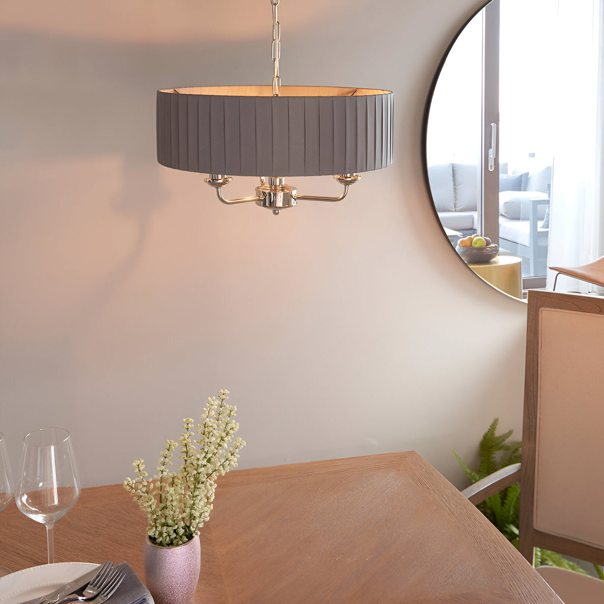 Brenley V2 3 Light Pendant in nickel with a pleated grey fabric drum shade, hung on a chain above a dining table near a round mirror.