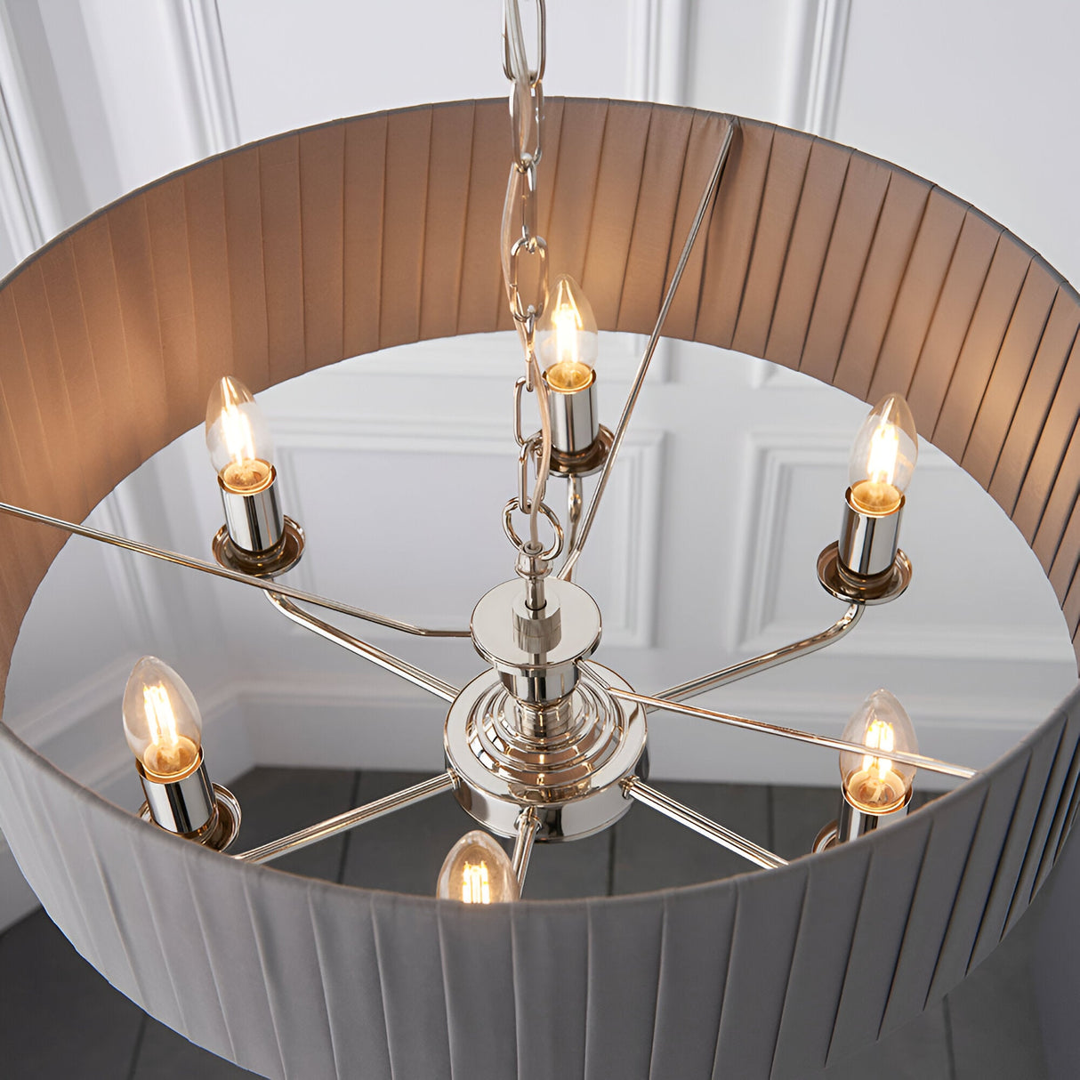 Brenley V1 six-light pendant with nickel and chrome candle-style holders and E14 bulbs beneath a pleated fabric drum shade, shown against a panelled wall.