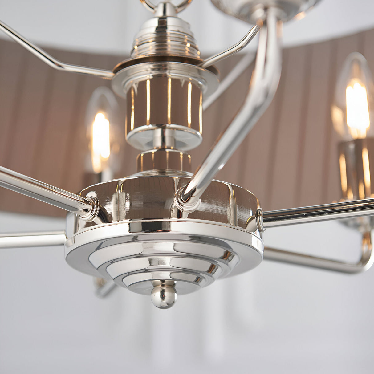 Close-up of the Brenley V1 6-light pendant's nickel and chrome hub showing tiered arms, candle bulbs, and fabric shades against a plain background.