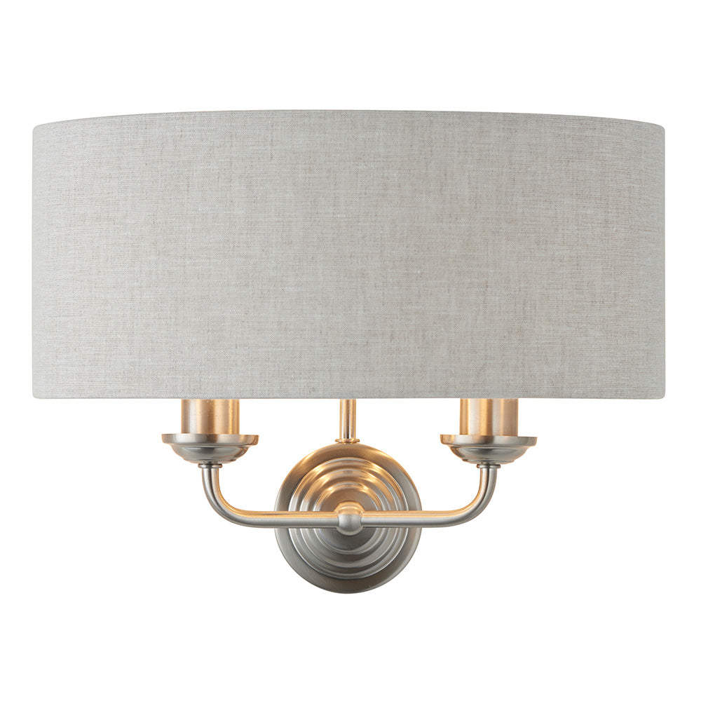 Brenley 2 Light Wall Light in chrome and brass with a light grey linen drum shade and twin candle-style arms, shown on a plain white background.