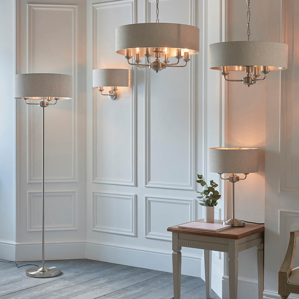 Brenley 2 Light Wall Light in chrome and brass with a linen drum shade, mounted on a panelled white wall beside pendant lights.