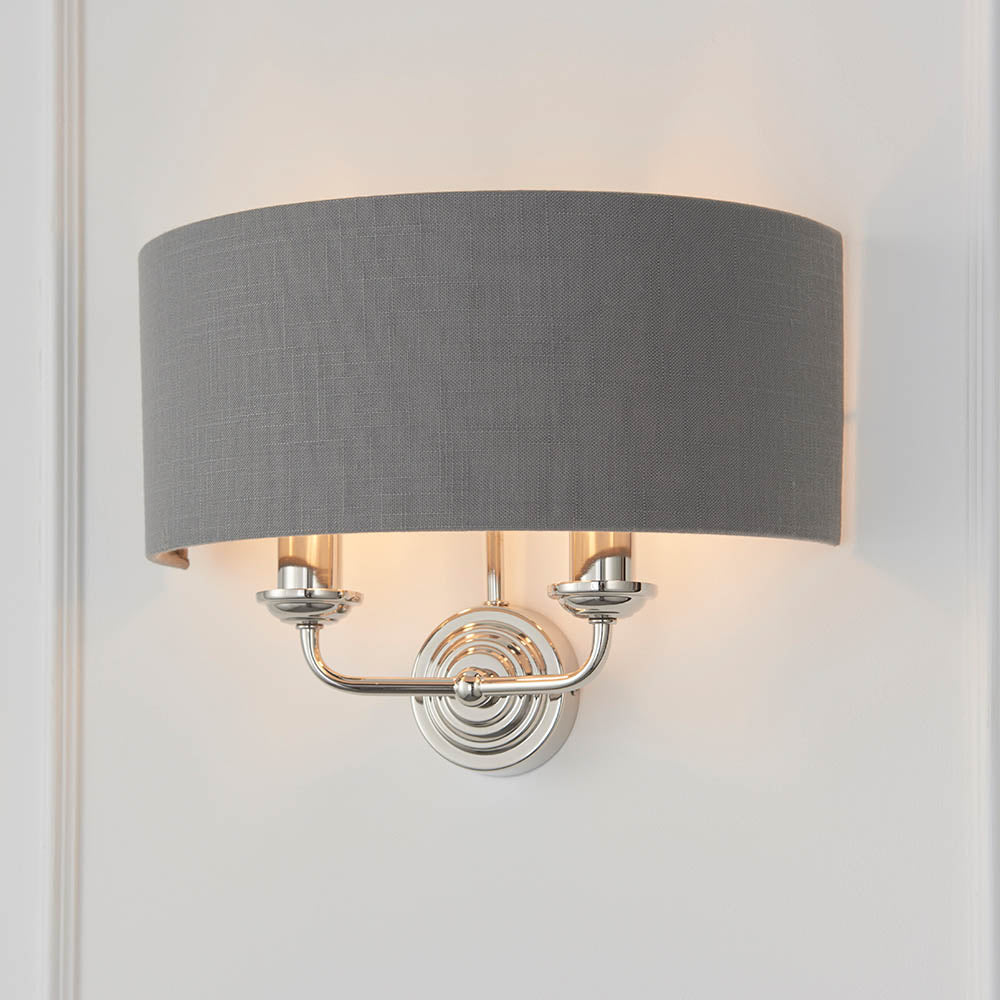 Brenley 2 Light Wall Light in nickel with a grey fabric drum shade and twin candle-style arms, mounted on a plain white wall.