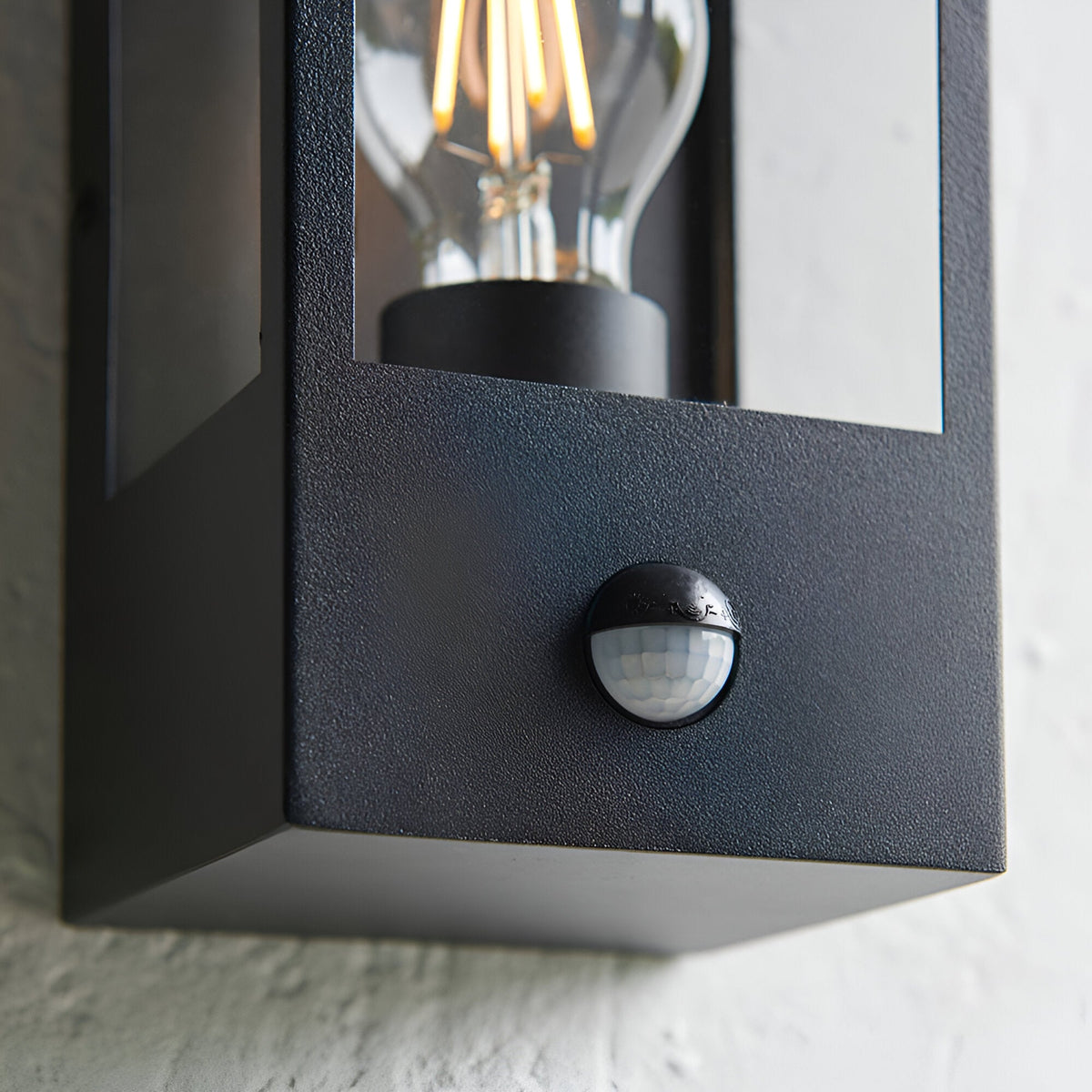 Close-up of the Castwood outdoor wall light in matt black steel with clear bevelled glass panel, integrated PIR sensor, and visible filament bulb.