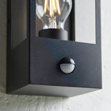 Close-up of the Castwood outdoor wall light in matt black steel with clear bevelled glass panel, integrated PIR sensor, and visible filament bulb.