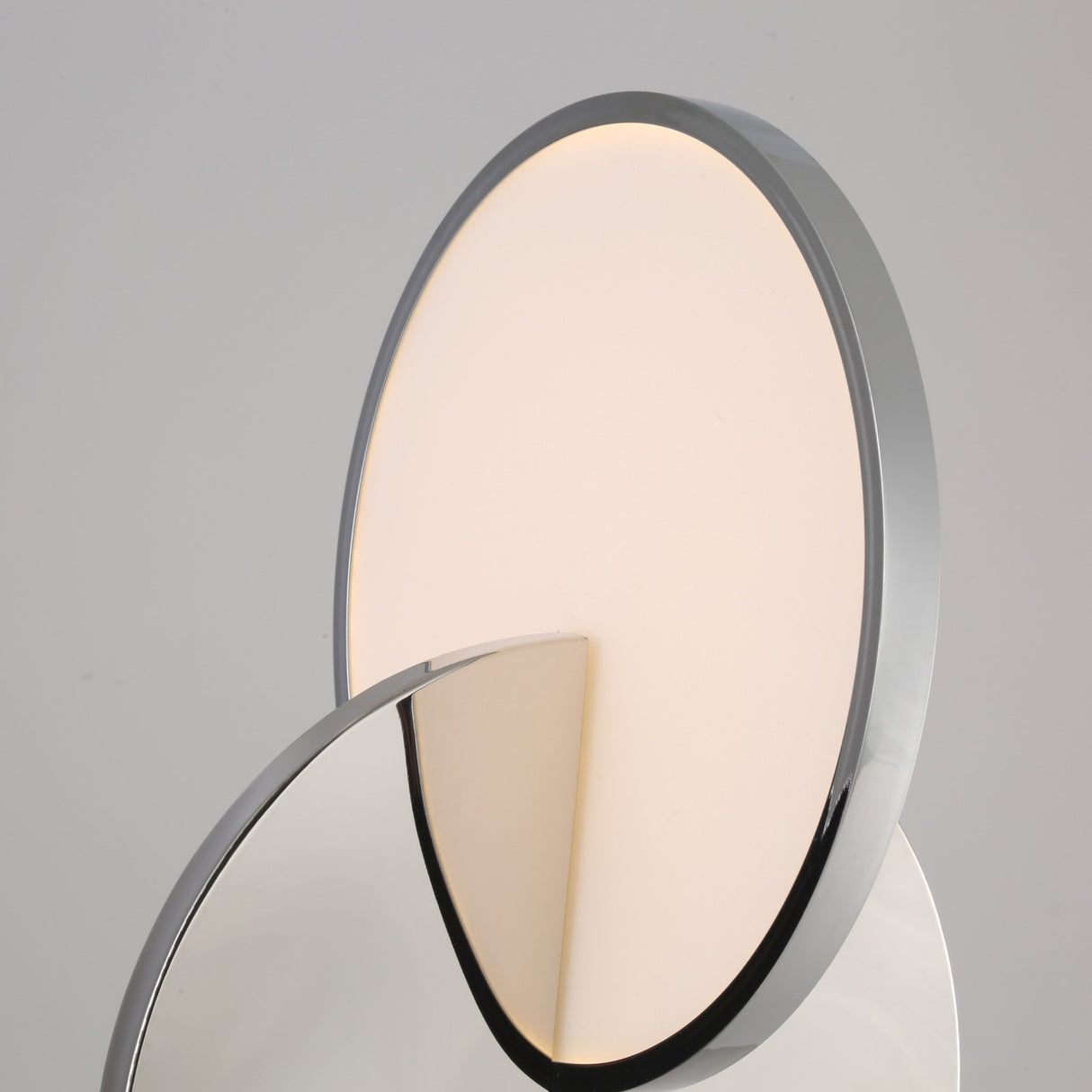 A close-up of the Half Moon LED Table Lamp - Silver, featuring a circular, softly glowing LED light and a reflective metallic front surface set against a plain background.