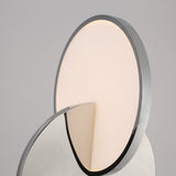 A close-up of the Half Moon LED Table Lamp - Silver, featuring a circular, softly glowing LED light and a reflective metallic front surface set against a plain background.