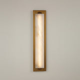 Valora vertical wall light with a tall natural alabaster panel glowing warm white, set in a brushed brass rectangular frame with brass fixings, on a plain light background.