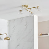 Denby 4 light semi-flush bathroom ceiling light in brass with clear glass shades, shown crossed on a white ceiling above marble-tiled shower fittings.