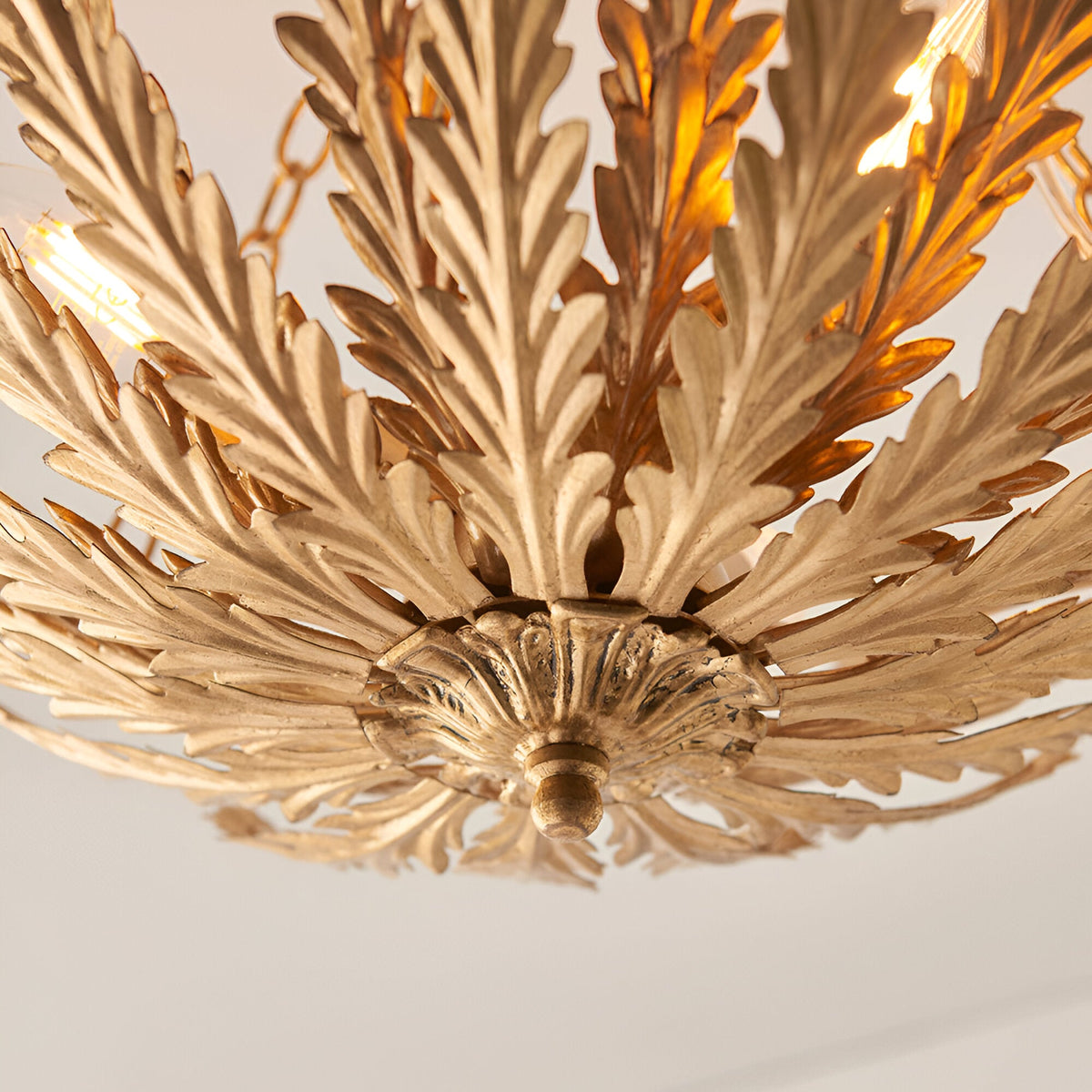 Close-up of Endon Colette 3 Light Flush Ceiling Light in gold, showing layered metal leaf detailing around the central mount with lit E14 lamps above.