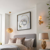 Colette Wall Light in gold leaf finish with layered leaf design and cream fabric shade, shown illuminated beside a bedroom wall.