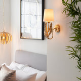 Colette Wall Light in gold with layered leaf detail and cream fabric shade, mounted above a bed in a bedroom setting.