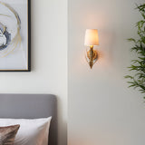 Colette Wall Light in gold leaf with layered leaf detail and cream fabric shade, mounted on a bedroom wall beside a framed artwork.
