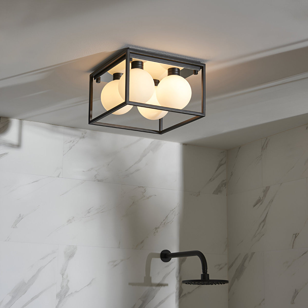 Endon Sable 4 light semi-flush bathroom ceiling light with matt black square cage frame and opal glass globes, mounted above a marble-tiled shower.