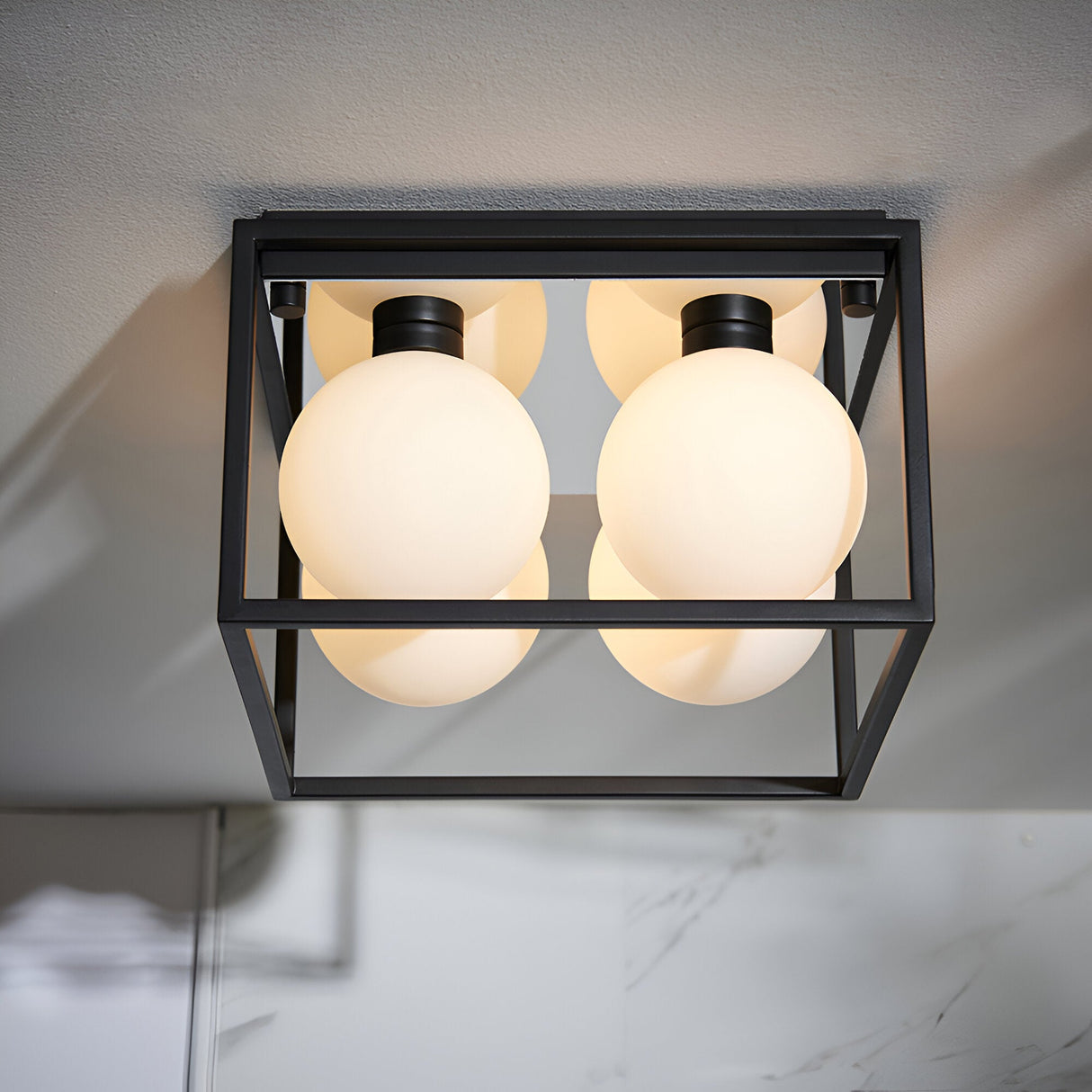 Endon Sable 4-light semi-flush bathroom ceiling light with matt black square cage frame and four white glass globe shades, mounted to a pale ceiling.