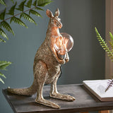 Endon Brockgrove Kangaroo table lamp in vintage silver resin, holding an exposed E27 filament bulb in a chrome holder, on a dark console with ferns.