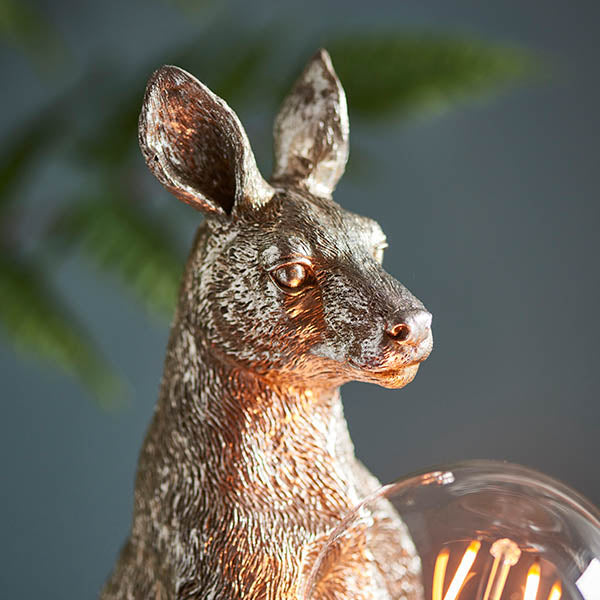 Endon Brockgrove kangaroo table lamp in vintage silver resin, close-up of the head and exposed E27 filament bulb against a dark foliage background.