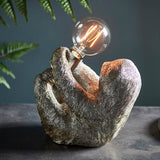Endon Cliffmont table lamp with a vintage silver resin sloth holding a chrome E27 holder and exposed globe bulb, on a grey surface beside ferns.