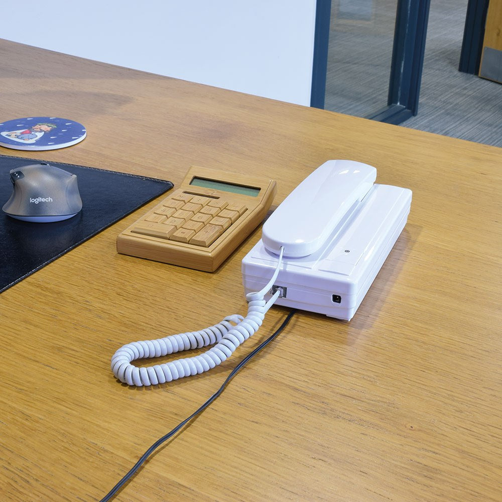 AVSL Mercury 2-Way Intercom unit in white plastic with lifted handset and coiled cord, shown on a wooden desk beside a bamboo calculator and mouse.