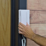 Hand lifting the white Mercury 2-Way Intercom handset from its wall-mounted base beside a wood-panelled door, coiled cable visible below.