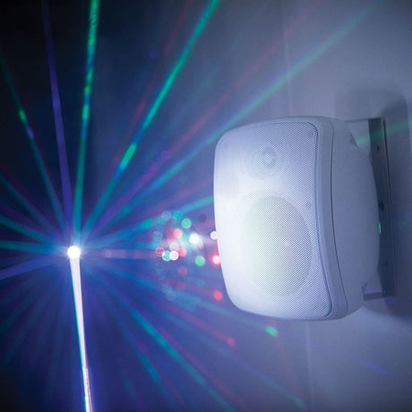 Adastra FC5V-W compact 100V background speaker in white, wall-mounted on a bracket with disco lighting casting colourful beams across the room.
