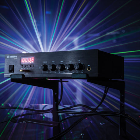 Adastra DM40 black mixer-amp with red LED display, USB slot, and treble, bass, MP3, aux and mic knobs, on a stand against a laser light backdrop.