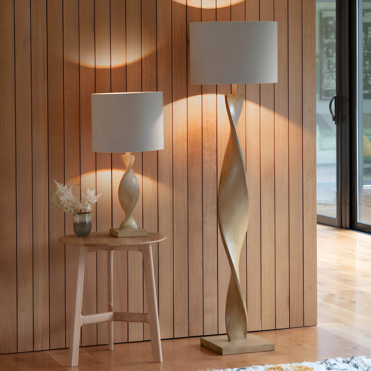 Endon Alcott floor lamp with spiral oak effect base and natural linen cylinder shade, beside a matching table lamp on a wooden side table.