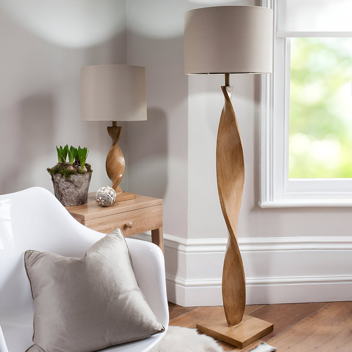 Endon Alcott floor lamp with spiral oak effect base and natural linen cylinder shade, beside a matching table lamp on an oak side table by a window.