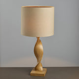 Alcott Table Lamp in Natural, featuring a spiral light oak-effect wood base and a cylindrical natural linen shade, set against a plain grey background.