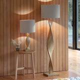 Alcott Table Lamp in natural oak-effect wood with a twisted spiral base and cylindrical linen shade, shown beside a matching floor lamp on a wooden side table.