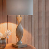 Alcott Table Lamp in Natural with twisted light oak-effect wood base and grey linen cylinder shade, lit on a wooden table against wood-panelled walls.