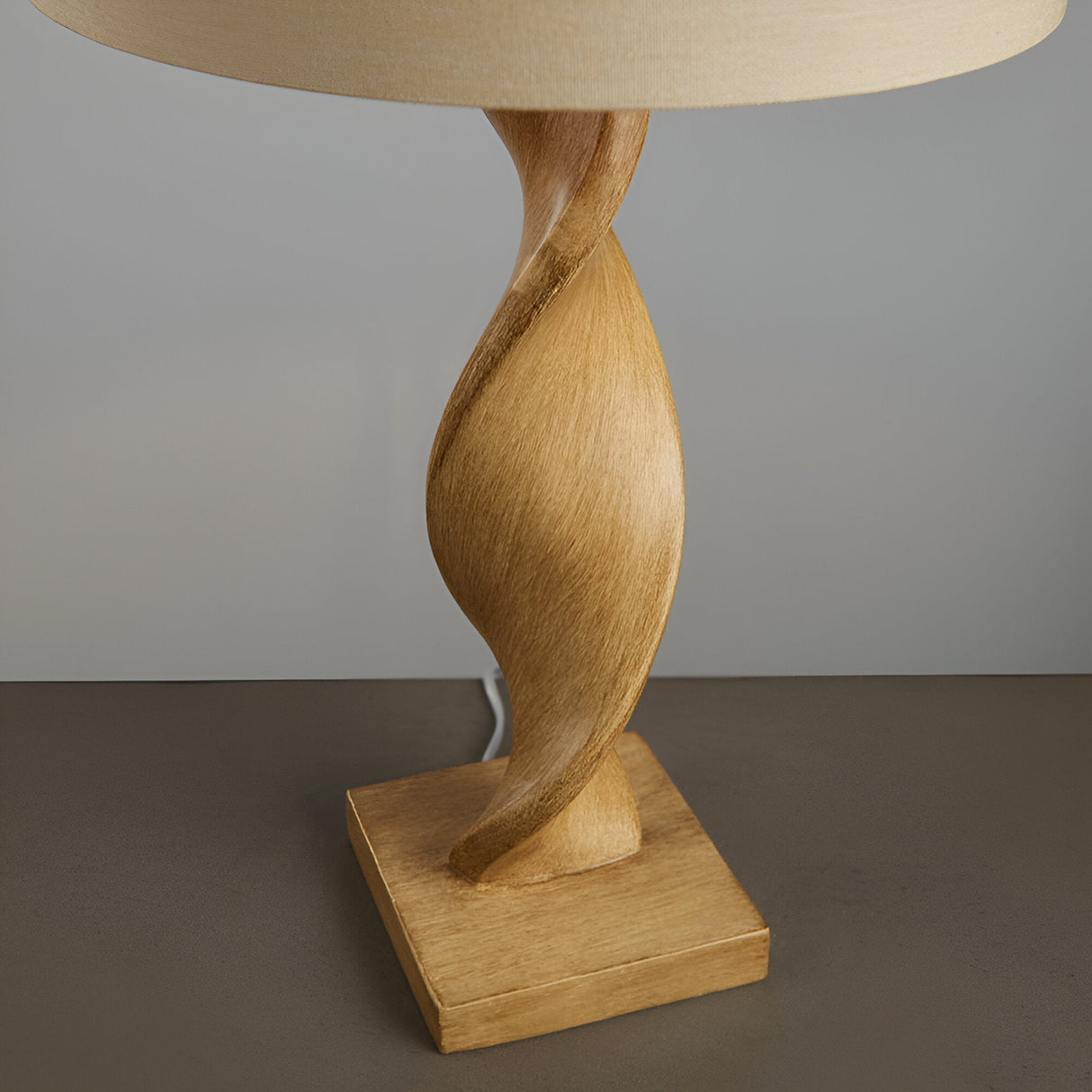 Alcott Table Lamp in Natural, showing the twisted spiral light oak base on a square plinth with a natural linen cylinder shade, against a plain grey background.