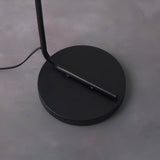 Cranmere Floor Lamp in matt black metal, close-up of angled pole and round base on a grey studio background.