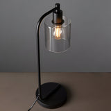 Endon Cranmere table lamp in matt black with an arched stem, round base, clear glass cylinder shade and exposed filament bulb on a neutral surface.